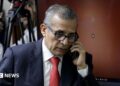 Ollanta Humala speaks on the phone as he leaves court in 2025. He wears a navy suit and red tie