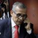 Ollanta Humala speaks on the phone as he leaves court in 2025. He wears a navy suit and red tie