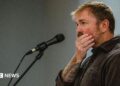 Graham Platner seen on stage at a microphone. his hand is over his mouth