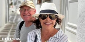 Karen Carter, pictured with her husband Alan. She is wearing dark glasses, a black and white sun hat and a white and striped shirt.