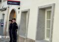 Two police officers stand outside a white-washed building with a police sign in German on the wall
