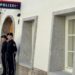 Two police officers stand outside a white-washed building with a police sign in German on the wall