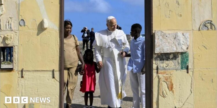 Pope Leo holds hands with a girl wearing a red dress and a man in blue shirt and white trousers. A women in a beige outfit stands alongside them at a doorway. Behind them are blue skies and men dressed in black