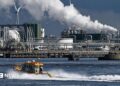 An oil refinery at the Port of Rotterdam. In the foreground a small boat leaves a wake in the water.