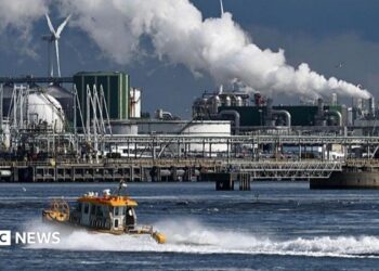 An oil refinery at the Port of Rotterdam. In the foreground a small boat leaves a wake in the water.