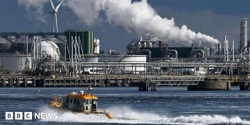 An oil refinery at the Port of Rotterdam. In the foreground a small boat leaves a wake in the water.