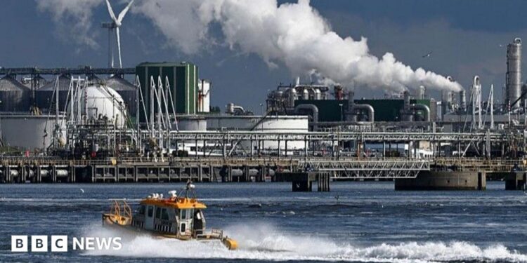 An oil refinery at the Port of Rotterdam. In the foreground a small boat leaves a wake in the water.
