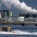 An oil refinery at the Port of Rotterdam. In the foreground a small boat leaves a wake in the water.