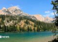 An aqua-blue river runs through a valley surrounded by pine trees and rocky mountains
