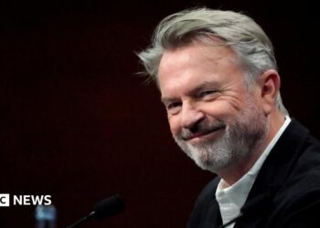 Sam Neill walking through a Jurassic forest, leading two children