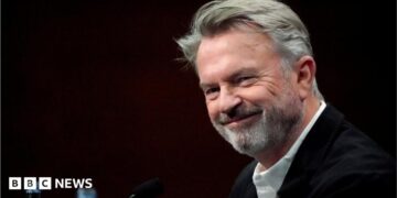 Sam Neill walking through a Jurassic forest, leading two children