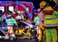 A number of emergency services personnel standing near an ambulance, with a person on a stretcher