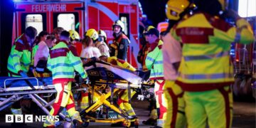 A number of emergency services personnel standing near an ambulance, with a person on a stretcher