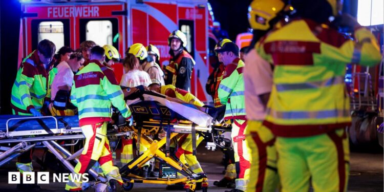 A number of emergency services personnel standing near an ambulance, with a person on a stretcher