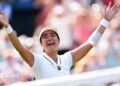 Filipina tennis player Alexandra Eala raises his arms after a Wimbledon match, net in front of her and a blurred image of the crowd in the background.