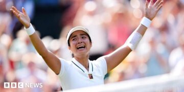 Filipina tennis player Alexandra Eala raises his arms after a Wimbledon match, net in front of her and a blurred image of the crowd in the background.