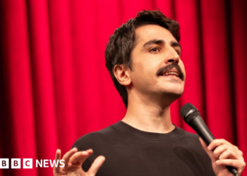 A head-shot posted by a Turkish stand-up comic showing him holding a microphone and standing in front of a red curtain