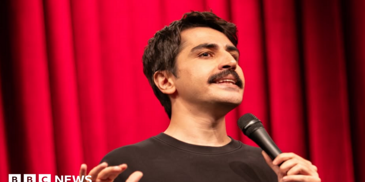 A head-shot posted by a Turkish stand-up comic showing him holding a microphone and standing in front of a red curtain