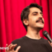 A head-shot posted by a Turkish stand-up comic showing him holding a microphone and standing in front of a red curtain