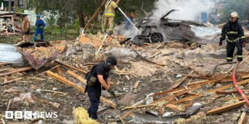 Emergency services clear through the rubble following a Russian missile strike just outside of Kyiv. Firefighters can be seen extinguishing a car fire in the background