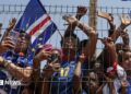 Fans wearing the Cape Verde kit press against a metal fence.