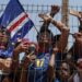 Fans wearing the Cape Verde kit press against a metal fence.