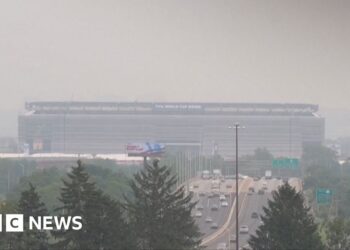 Smoke from Canadian wildfires shrouds MetLife Stadium, host of the 2026 FIFA World Cup final, as hazy orange skies reduce visibility over a busy highway in New Jersey.