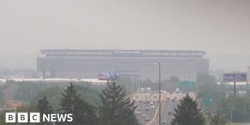Smoke from Canadian wildfires shrouds MetLife Stadium, host of the 2026 FIFA World Cup final, as hazy orange skies reduce visibility over a busy highway in New Jersey.