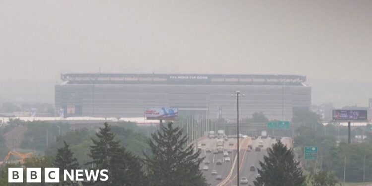 Smoke from Canadian wildfires shrouds MetLife Stadium, host of the 2026 FIFA World Cup final, as hazy orange skies reduce visibility over a busy highway in New Jersey.