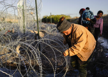 A group of migrants make their way along miles of concertina wire deployed by the Texas National Guard under Operation Lone Star in El Paso, Texas on April 2, 2024.