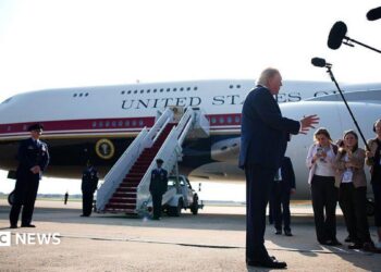 Trump stands in front of Qatari-gifted Air Force One and speaks to reporters who are holding boom microphones