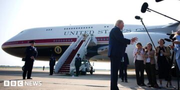 Trump stands in front of Qatari-gifted Air Force One and speaks to reporters who are holding boom microphones