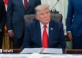 US President Donald Trump sitting in the White House wearing a blue suit jacket, white shirt and red tie.