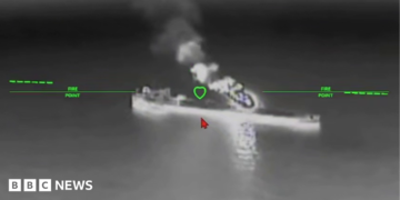 A still image of an oil tanker under attack from a drone in a black and while nighttime image