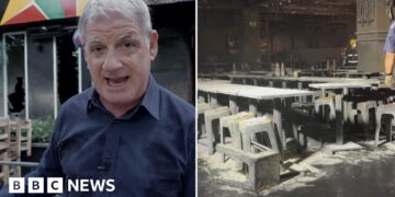 A man speaking in front of a building, and on the right the inside of a burned building with tables and chairs.