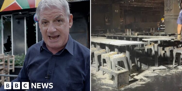 A man speaking in front of a building, and on the right the inside of a burned building with tables and chairs.