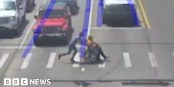 Man dressed as Spider-Man pushes wheelchair user across a crossing