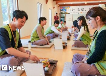 A row of men sitting and a row of women sitting on the floor of a temple across from each other