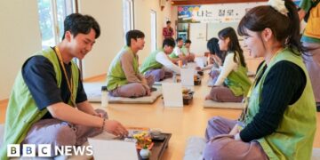 A row of men sitting and a row of women sitting on the floor of a temple across from each other