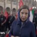 Lyse Doucet looks into the camera as she stands among a crowd carrying Iranian flags