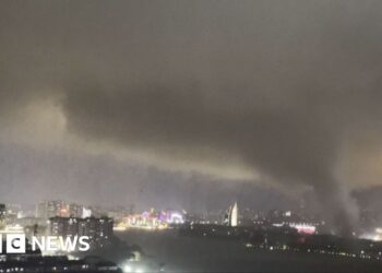 A giant tornado sweeping a city in the night, with the skyline of a city behind it