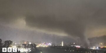 A giant tornado sweeping a city in the night, with the skyline of a city behind it