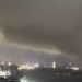 A giant tornado sweeping a city in the night, with the skyline of a city behind it