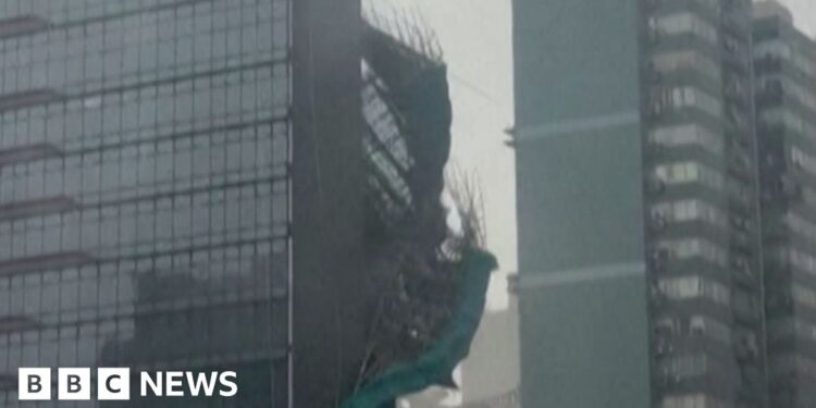 Bamboo and green plastic sheeting are seen falling down the side of a glass skyscraper.