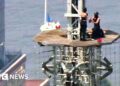 A man and a woman are seen during a proposal on top of the top of the Empire State Building.