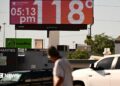 Man walks through road and looks up at sign that says 118 degrees and 05:15 pm