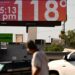 Man walks through road and looks up at sign that says 118 degrees and 05:15 pm