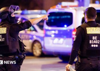 A police officer carrying a machine gun (L) and a colleague talk near the scene where several people were injured on the sideline of the Christopher Street Day (CSD) parade in Berlin, Germany, 25 July 2026.