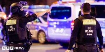 A police officer carrying a machine gun (L) and a colleague talk near the scene where several people were injured on the sideline of the Christopher Street Day (CSD) parade in Berlin, Germany, 25 July 2026.