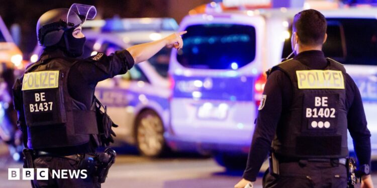 A police officer carrying a machine gun (L) and a colleague talk near the scene where several people were injured on the sideline of the Christopher Street Day (CSD) parade in Berlin, Germany, 25 July 2026.